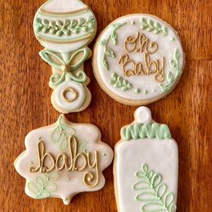 Pu&ograve; includere: Quattro biscotti di zucchero decorati con glassa verde e oro. I biscotti hanno la forma di un sonaglio, un biberon, un cerchio e uno stendardo. Il biscotto rotondo ha le parole "Oh Baby" scritte su di esso. Il biscotto a forma di stendardo ha la parola "baby" scritta su di esso.