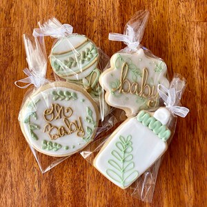 Pu&ograve; includere: Quattro biscotti di zucchero decorati in sacchetti di cellophane individuali. I biscotti sono decorati con glassa verde e oro. I biscotti mostrano le parole "One Baby", "Baby", uno sonaglio e un biberon.