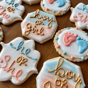 Puede incluir: Un conjunto de seis galletas de revelaci&oacute;n de g&eacute;nero decoradas con glaseado azul y rosa. Las galletas presentan las frases "boy or girl", "he or she" y huellas.