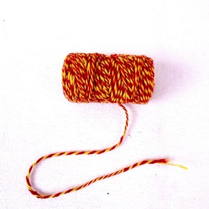 Puede incluir: Un rollo de cuerda roja y amarilla con un hilo largo de cuerda que se extiende desde el rollo.