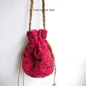 Peut inclure: Un sac en velours rose fuchsia avec des ornements de perles dorées en forme de losanges. Le sac a une poignée tressée en perles dorées et une fermeture à cordon. Le texte "Craft Colours India" est visible sur l'image.