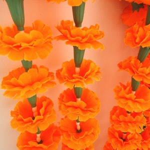 Puede incluir: Primer plano de guirnaldas de flores de cal&eacute;ndula de color naranja vibrante. Cada guirnalda presenta m&uacute;ltiples flores de color naranja brillante con tallos verdes. Las guirnaldas probablemente se utilizan para la decoraci&oacute;n o ceremonias religiosas.