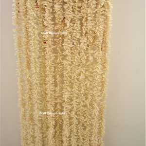 May include: A white garland made of paper flowers, hanging in a doorway. The garland is made of many strands of paper flowers, and it is hanging from the top of the doorway. The garland is decorated with the text "Craft Colours India".