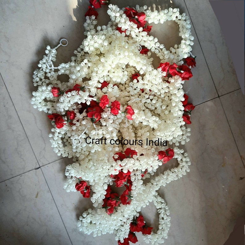 May include: A white garland of artificial flowers with red flower accents. The garland is made of small, round, white flowers and is strung together with a thin, white string. The garland is perfect for adding a touch of elegance to any occasion.