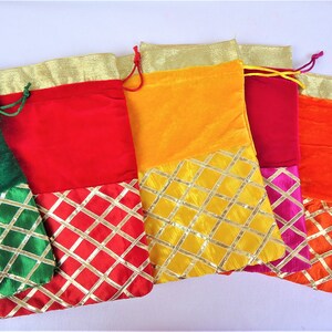 May include: Five colorful drawstring bags with gold trim and a diamond pattern. The bags are made of velvet and have a contrasting fabric bottom. The colors are green, red, yellow, burgundy, and orange.