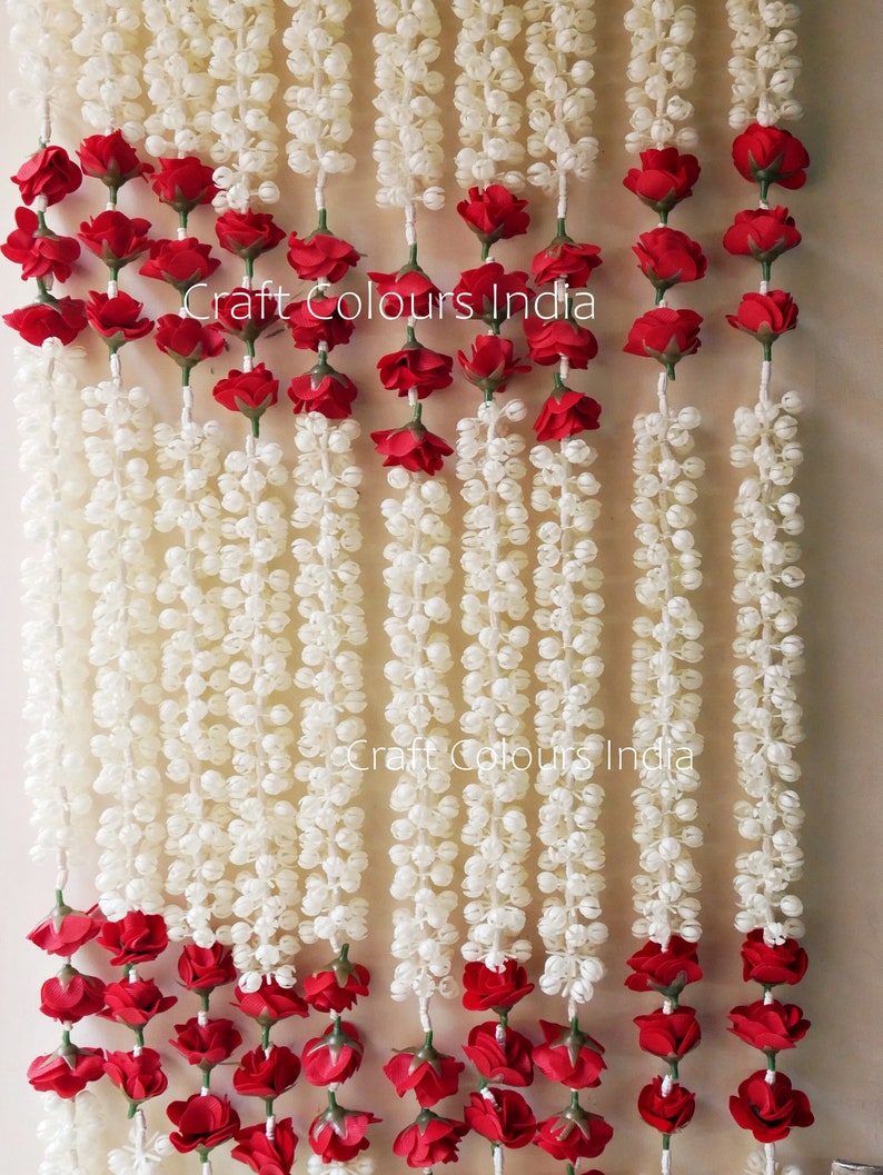 May include: A garland of white jasmine flowers with red rose accents. The garland is made of artificial flowers and is perfect for decorating for a wedding or other special occasion. Craft Colours India.
