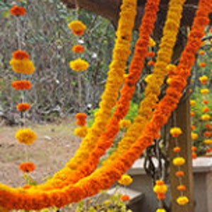 May include: A garland of orange and yellow marigold flowers, strung together and hanging from a wooden structure. The garland is used for decoration and is a traditional element in Indian weddings and festivals.