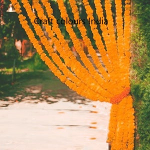 May include: A close-up of a doorway decorated with marigold flower garlands. The garlands are strung together in rows and hang from the top of the doorway. The flowers are a bright orange colour and create a festive atmosphere.