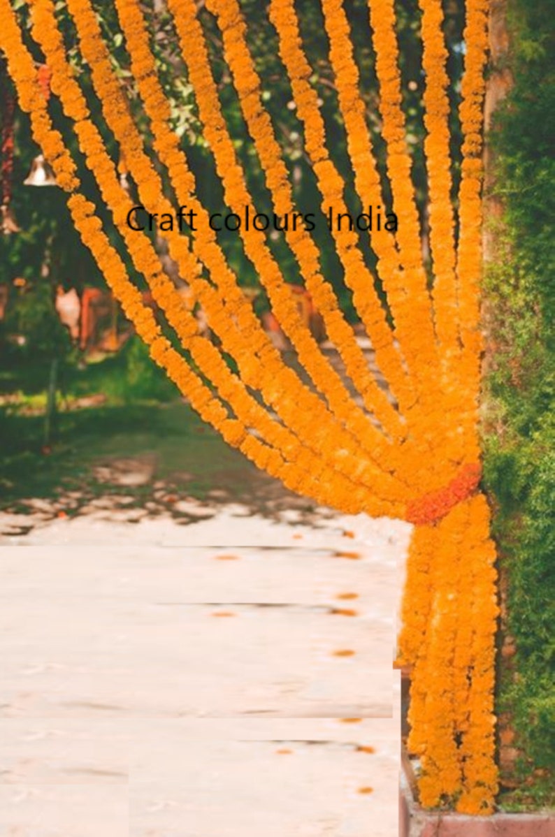 May include: A close-up of a doorway decorated with marigold flower garlands. The garlands are strung together in rows and hang from the top of the doorway. The flowers are a bright orange colour and create a festive atmosphere.