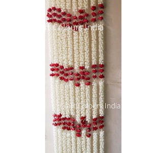 May include: White flower garlands with red rose accents, hanging in a doorway. The garlands are made of artificial flowers and are strung together with a wire. The text "Craft Colours India" is visible in the image.
