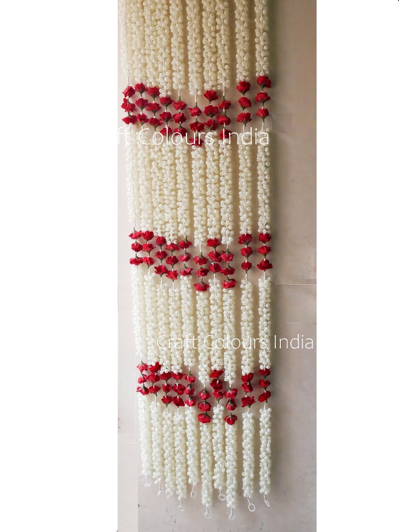 May include: White flower garlands with red rose accents, hanging in a doorway. The garlands are made of artificial flowers and are strung together with a wire. The text "Craft Colours India" is visible in the image.