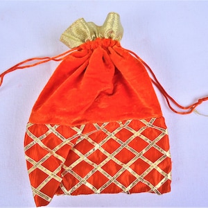 May include: Orange velvet drawstring bag with gold trim and a diamond pattern. The bag is closed with a drawstring.
