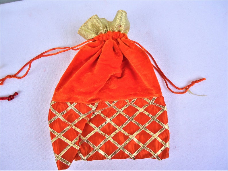 May include: Orange velvet drawstring bag with gold trim and a diamond pattern. The bag is closed with a drawstring.