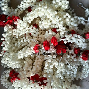 May include: A garland of white plastic flowers with red rose accents. The garland is made of small, round, white plastic flowers that resemble jasmine blossoms. The garland is perfect for adding a touch of elegance to any occasion.