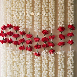 May include: White and red artificial flower garland with the text "Craft Colours India" printed twice. The garland is made of small white balls and red roses.