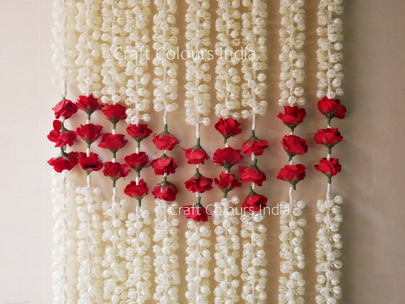 May include: White and red artificial flower garland with the text "Craft Colours India" printed twice. The garland is made of small white balls and red roses.