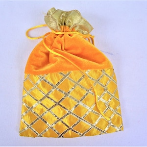 May include: A yellow velvet drawstring bag with a gold patterned bottom. The bag is closed with a gold drawstring.