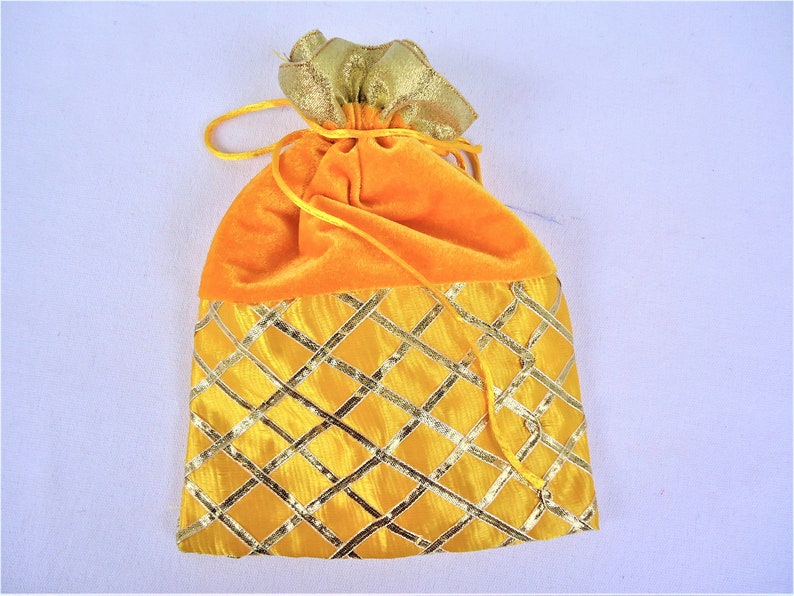 May include: A yellow velvet drawstring bag with a gold patterned bottom. The bag is closed with a gold drawstring.