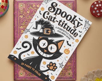 May include: A Halloween-themed coloring book titled "Spooky Cat-titude" featuring a cartoon black cat wearing a witch hat. The cover includes pumpkins, bats, and spiderwebs. The book is on top of a purple, ornate journal.