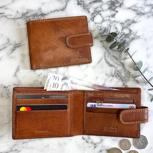 May include: Two brown leather wallets, one closed and one open, showing banknotes, credit cards, and a UK driving licence. The open wallet displays the text "Hand Made Fine Leather" and "RFID PROTECTED".