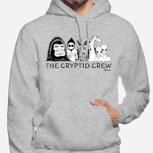 May include: A gray hooded sweatshirt with a black and white illustration of a group of cryptids, including a gorilla, a ghost, a mothman, a giraffe, and an alien. The text "THE CRYPTID CREW" is printed below the illustration.