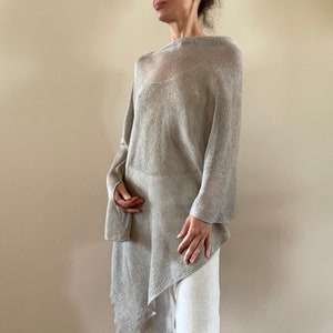 Könnte beinhalten: Ein hellgraues, durchsichtiges, gestricktes Poncho mit einem drapierten, asymmetrischen Saum.