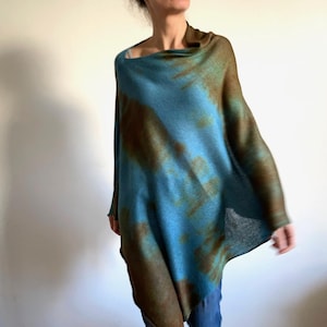 Puede incluir: Un poncho de punto azul y marrón con estampado tie-dye y cuello drapeado.