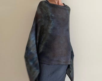 May include: A dark, mottled poncho featuring a blend of deep charcoal, navy blue, and subtle forest green tones. The garment has a wide, draped silhouette with a textured knit surface, creating a soft, flowing appearance that hangs loosely over the shoulders.