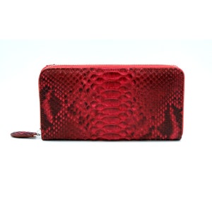Puede incluir: Una cartera de piel de serpiente roja con cierre de cremallera.