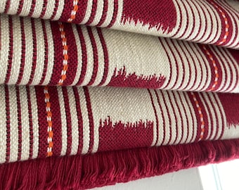 May include: Red and beige striped fabric with a fringe trim. The fabric has a woven pattern with red and orange stripes.