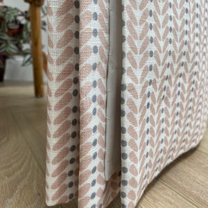 May include: Close-up of a pink and grey patterned fabric with a geometric design. The fabric is folded and shows the seams.