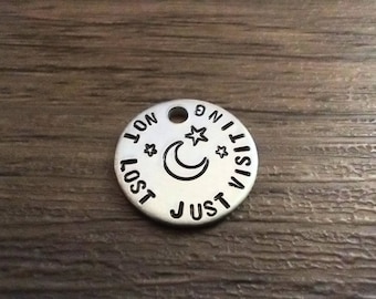 May include: Silver charm featuring a crescent moon and stars, with the inscription "I lost just visiting on", a common design for jewellery making.