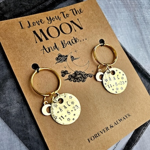 May include: A brown card with the text "I Love You To The Moon And Back..." and two gold keychains with a moon and star charm. The charms are engraved with "A & C 11.5.23". The card also has the text "FOREVER & ALWAYS."