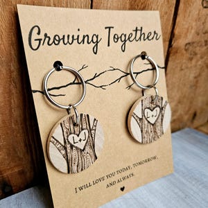 May include: Two wooden keychains with a tree design and a heart with the initials "L+J" inside. The keychains are attached to a card that reads "Growing Together" and "I will love you today, tomorrow, and always."