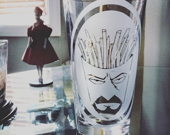 May include: A clear glass beer mug with a white design of a cartoon face with a mustache and eyebrows. The face is surrounded by a circle of white french fries.