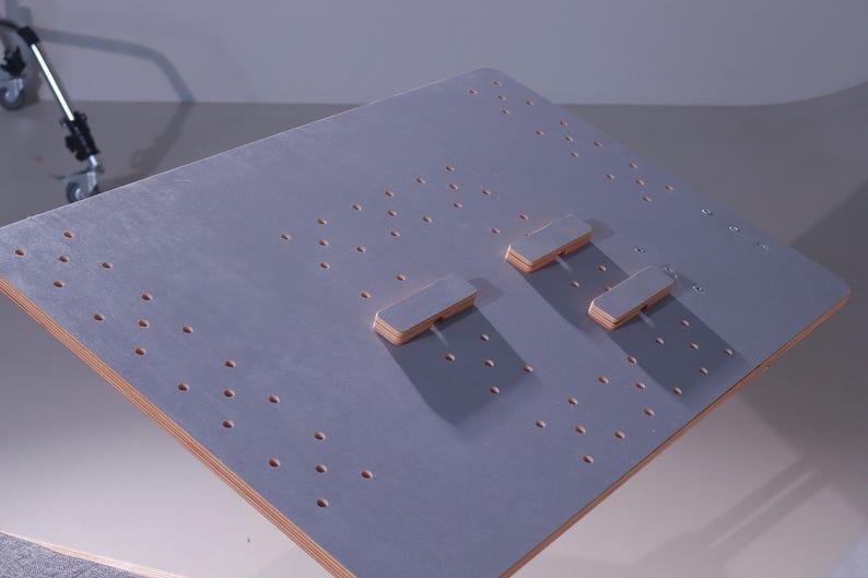 May include: A gray wooden board with numerous small holes and three rectangular wooden blocks. The edges of the board are a natural wood color. The board is likely a component of a larger structure or a specialized work surface.