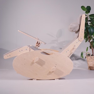 May include: A light-colored wooden rocking chair with a built-in desk and headrest. The chair has a curved base and a reclining back. The headrest and seat are upholstered in a light gray fabric. The chair is designed for comfort and relaxation.
