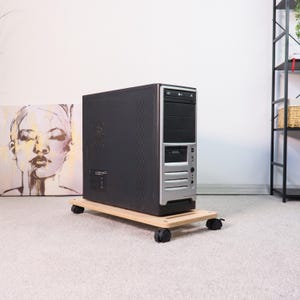 May include: A black and silver computer tower on a light wood rolling cart with black wheels. The computer case has a silver front panel with multiple drive bays and a power button. The cart is rectangular and sits on a carpeted floor.