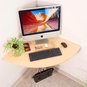 May include: A light wood corner desk with a computer monitor, keyboard, mouse, and two mobile phones. A black handbag hangs from the underside of the desk.