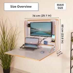 May include: A wall-mounted fold-down desk with a light wood frame and white surface. Text reads Size Overview and MAXI SIZE. Dimensions are 29.1 inches wide, 23.6 inches high, and 5.9 inches deep. It holds a monitor, laptop, and phone.