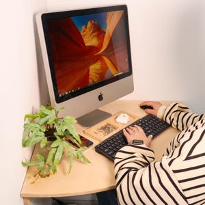 Könnte beinhalten: Eine Person arbeitet an einem Holztisch mit einem Computer, einer Tastatur und einer Maus. Der Bildschirm des Computers zeigt ein Landschaftsbild eines Canyons.