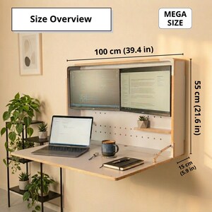 May include: A wall-mounted wooden desk with a fold-down surface, featuring two monitors, a laptop, and a small shelf. Text labels indicate dimensions of 39.4 inches wide, 21.6 inches high, and 5.9 inches deep. The unit includes a pegboard back panel.