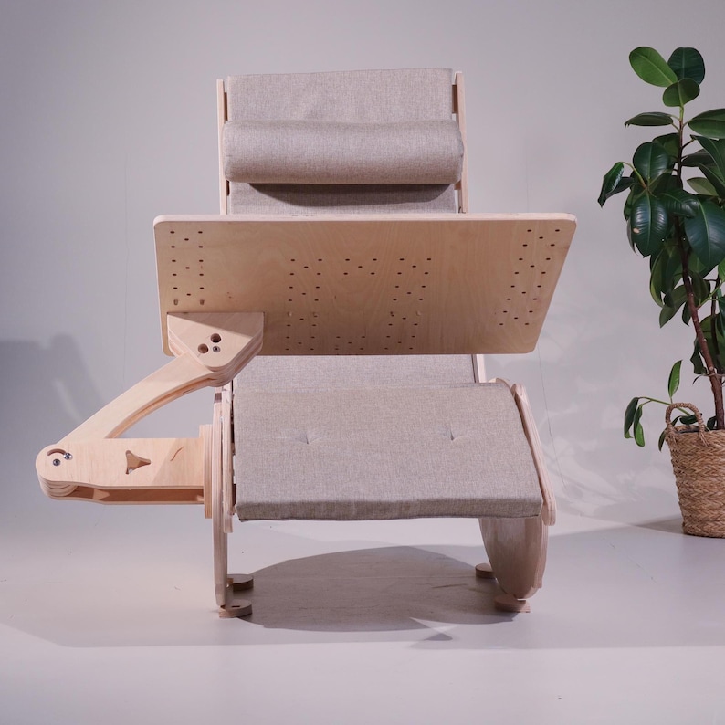 May include: A light wood rocking chair with a built-in desk. The chair has a light gray upholstered seat, back, and headrest. The desk is made of light wood and has several small holes. The chair is designed for comfort and functionality.