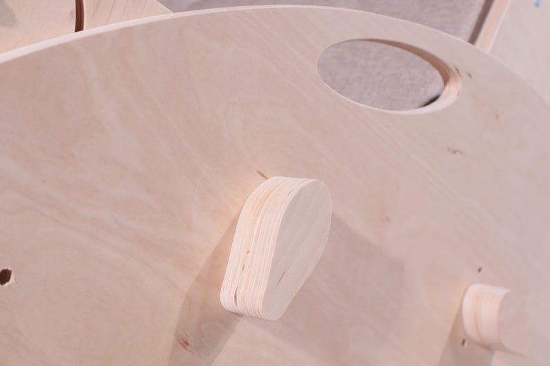 K&ouml;nnte beinhalten: Nahaufnahme eines hellfarbenen Holzobjekts mit abgerundeter Form und einem kreisf&ouml;rmigen Ausschnitt. Das Objekt hat eine nat&uuml;rliche Holzmaserung und mehrere angebrachte Holzteile. Das Design scheint Teil einer gr&ouml;&szlig;eren Struktur zu sein.