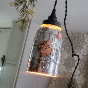 May include: A silver and copper patterned glass jar pendant light fixture with a black cord hanging from the ceiling.