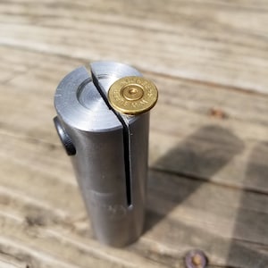 Könnte beinhalten: Ein silbernes Werkzeug aus Metall mit einer geteilten Oberseite, das für die Aufnahme einer verbrauchten .44 Magnum-Hülsen verwendet wird. Die Hülse ist oben im Werkzeug sichtbar.