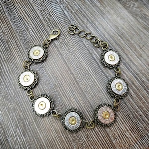 May include: A silver and gold bracelet with a chain and seven round charms. Each charm is a spent bullet casing with the words "Winchester" and "Auto" engraved on them.