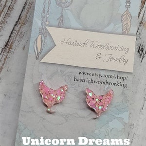May include: A pair of pink glitter chicken earrings with the text "Unicorn Dreams" and the shop name "Hastrich Woodworking & Jewelry" and website address "www.etsy.com/shop/hastrichwoodworking".