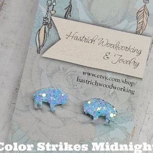 May include: A pair of blue glitter buffalo earrings on a white card with the text "Color Strikes Midnight" and the shop name "Hastrich Woodworking & Jewelry" with a website address.