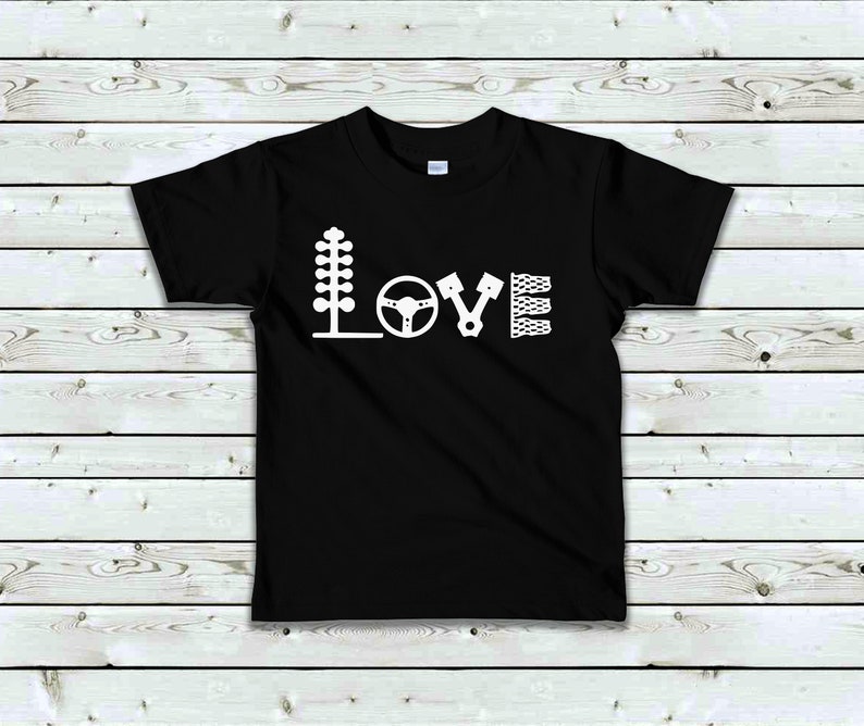 May include: Black t-shirt with a white graphic of the word "LOVE" spelled out using racing-themed icons. The icons include a Christmas tree, a steering wheel, a piston, and a chequered flag.